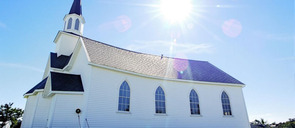 Bright sky, green grass, brick building, tall steeple