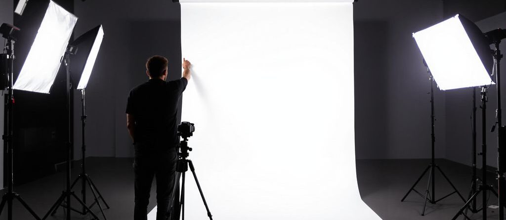 Photographer adjusting large white backdrop with lights.