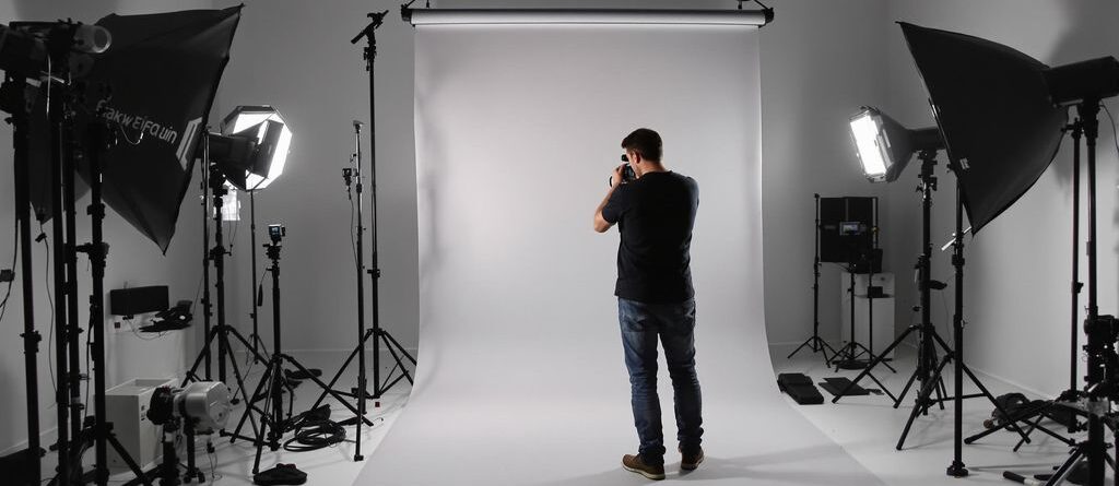 Photographer adjusts portable backdrop stand in studio.